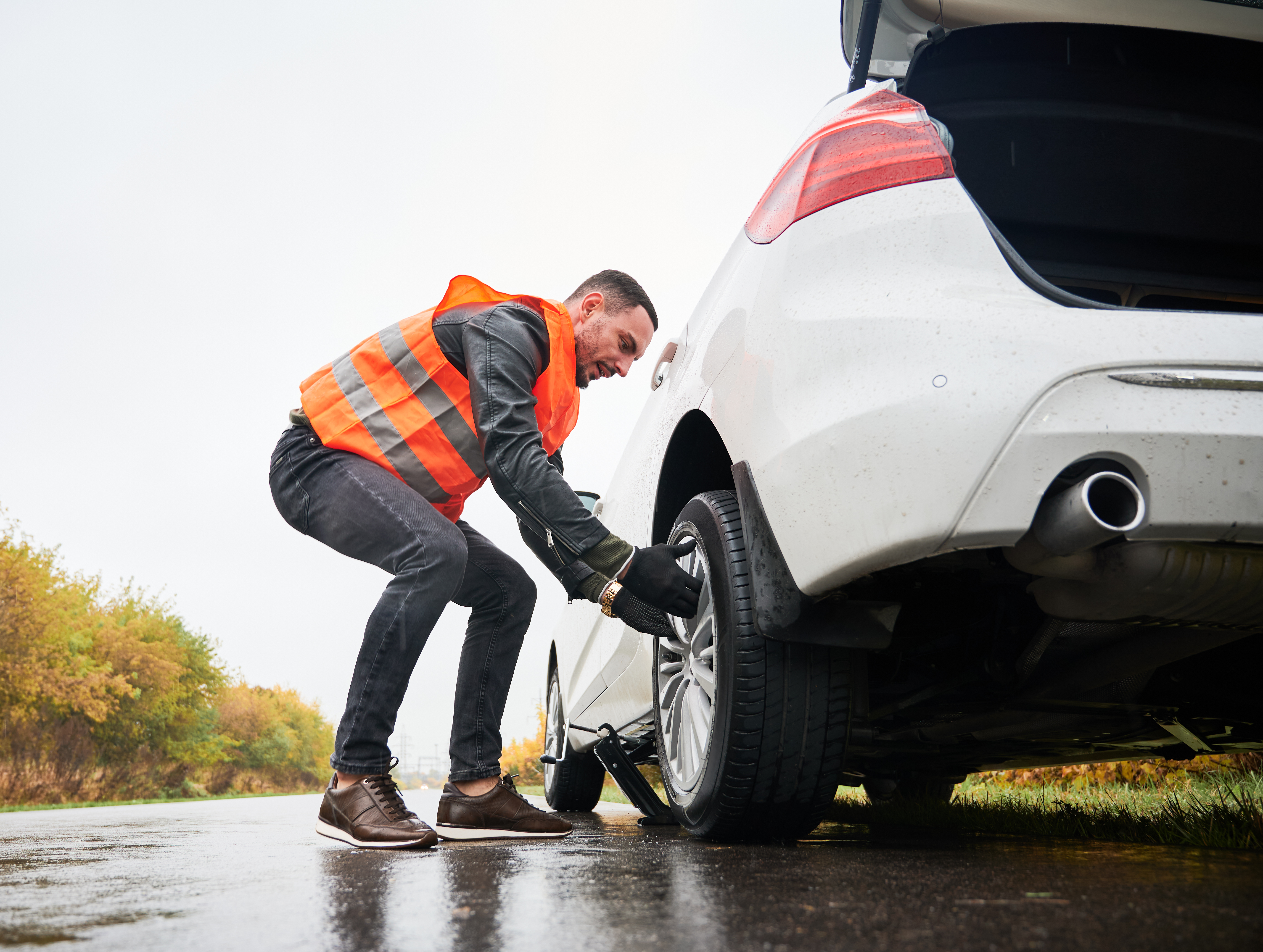 Roadside assistance worker removing flat tire while repairing car on the street. Male auto mechanic in work vest changing flat tire on the road. Concept of emergency road service.