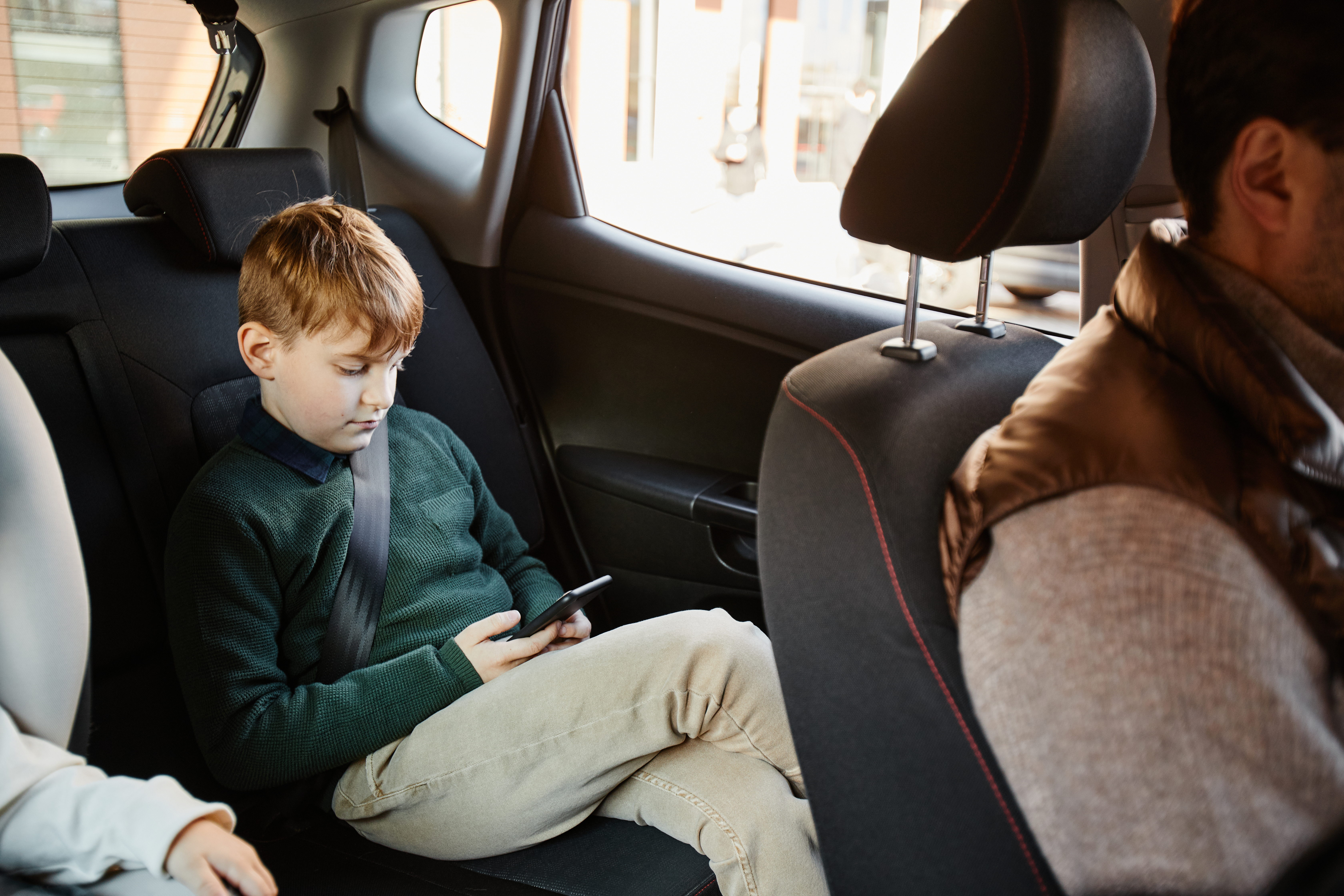 Portrait of boy in back seat of family car using smartphone and playing mobile game, copy space